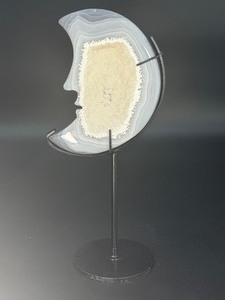 lot 11 image: A luminous Botswana Agate druzy carved into a moon shape, showcasing delicate bands of soft gray, caramel, and cream. The sparkling druzy surface catches the light, in a custom metal stand. 6.6 oz.  0.188 kg.