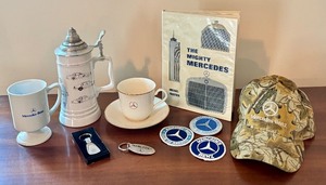 lot 117 image: Mercedes-Benz Collectibles Set with Mugs, Patches, Book, Hat, and Keychains