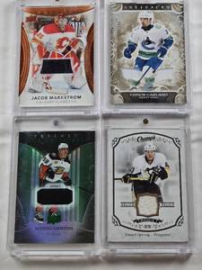 lot 114 image: Conor Garland 2024-25 Upper Deck Artifacts Patch 170299, Daniel Sprong 2015-16 Upper Deck Champs Rookie Relic, Jacob Markstrom 2022-23 Upper Deck Trilogy Black Patch, Maxime Comtois 2018-19 Upper Deck Trilogy Rookie Premieres Patch 451499