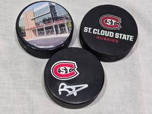 lot 38 image: Ryan Poehling Autographed St. Cloud State Huskies Hockey Puck with 2 other Pucks including NCHC Official Game Puck and Herb Brooks National Hockey Center Commemorative Puck