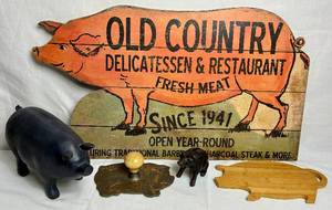 lot 125 image: Primitive Pig Bundle - Cast Iron Piggy Bank , Bacon Press, Old Country Delicatessen & Restaurant Sign (30 W) and 11.5 Black Pig Sculpture