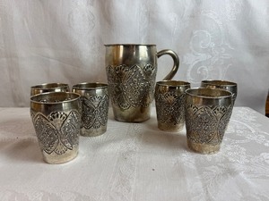 lot 233 image: Antique Silver Drinkware Set includes Pitcher and Six Glasses featuring Intricate Embossed Floral Design (Silver marking on bottom of each piece)