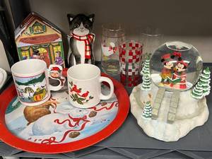 lot 123 image: Holiday Decor Collection with Mickey and Minnie Snow Globe, Cat Figurine, Christmas Tin, Mugs, and Glassware