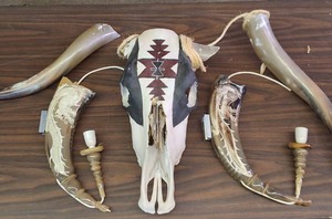 lot 320 image: This item is a decorative collectible hand-painted cow skull adorned with Native American-inspired artwork and associated horn accessories.