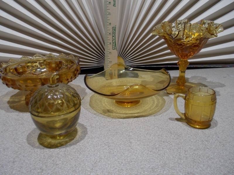 lot 116 image: The image displays a collection of vintage amber glass items, including a ruffled compote, a basket dish, a covered candy dish, and a small mug