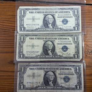 lot 310 image: Lot of 3 Notes  Series 1957A 1957D 1957D  $1 Silver Certificates in circulated condition, Blue Seal