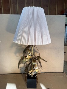 This Lot is a 1970s Hollywood Regency-style table lamp, featuring a sculpted metal base and a pleated shade
