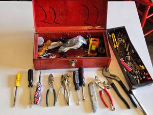 Red metal toolbox with assorted hand tools and accessories including pliers, screwdrivers, a utility knife, and a socket set