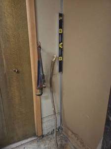 a level tool, pipe wrench, and a long wooden stick leaning