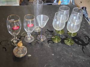 Mixed glassware including Stella Artois glasses, wine glasses with green stems, and a decorative bottle with a crown top.
