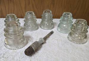 Six vintage clear glass insulators, specifically resembling the Hemingray-45 model based on their shape and color and a pin glass insulator.&nbsp