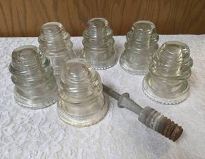 Six vintage clear glass insulators, specifically resembling the Hemingray-45 model based on their shape and color and a pin glass insulator.&nbsp