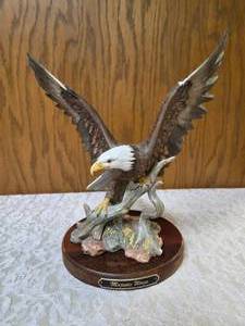 Homco Majestic Wings bald10 eagle figurine. It is a porcelain sculpture depicting a bald eagle landing on a rocky mound and is mounted on a dark wooden base with a plaque reading Majestic Wings.&nbsp There is some paint missing on the wings.