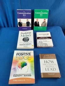 Collection of six self-improvement, financial literacy, leadership, and communication books laid out on a blue fabric surface.