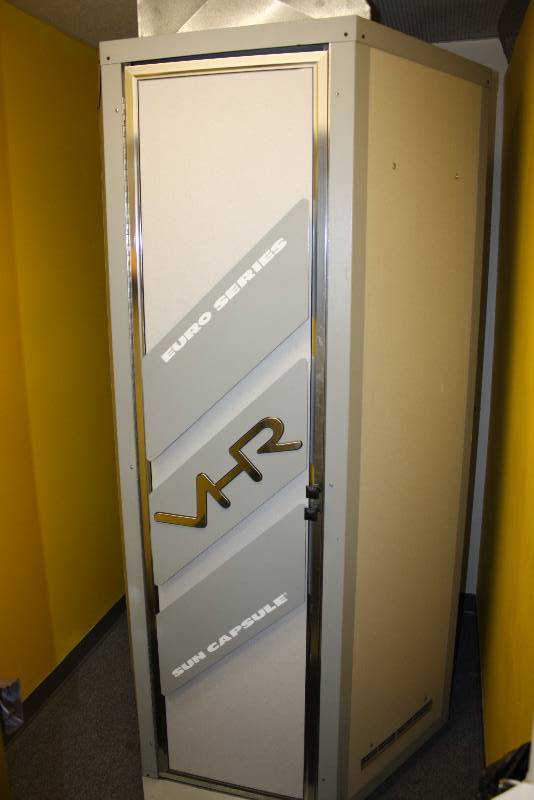 lot 2 image: Room Lot Including VHR Sun Capsule Tanning Booth Serial No. 003232, Model SC I VHR, Standing Style 48 x48 x 84 Wooden Shelf, 24 x 7 Wall-Mount Garbage Can, 14  x7 x 4 Requires Tools For Removal.