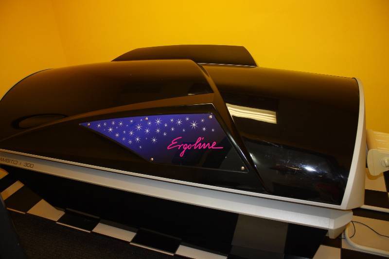 lot 13 image: Room Lot Including Ergoline Ambition 300 Tanning Booth Unknown Hours Canopy Style Curved WCords Dimensions Tanning Bed 91 x 46 x 40 Decorative Floor RunnerRug, 84 x 24 Glass Shelf 25 x 8 Wall Mount Garbage Can 14 x 7 x4