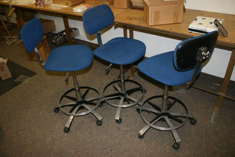 lot 1107 image: Chair Lot Including Blue Backed Chairs wBases Wooden Stool Office Chair And More Includes All Chairs In Work Room.