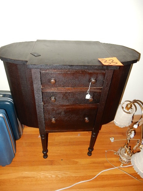 lot 33 image: Sewing Cabinet.. Has side storage flip tops.. 3 drawers.  27 in w x 14 in d x 28in h.  Not sure of wood. .DARK stained.