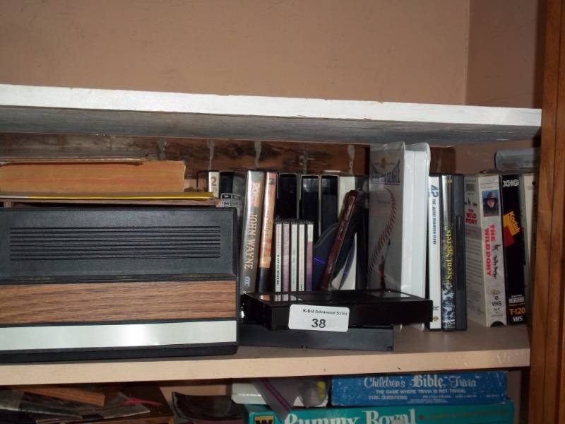 lot 38 image: Shelf of VHS movies with VHS holder and misl contents.
